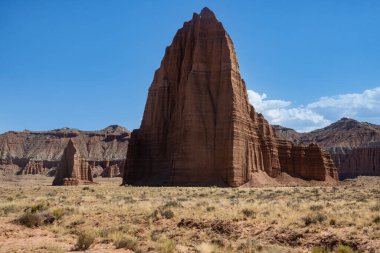 Utah, ABD 'deki Capital Reef Ulusal Parkı' nda çarpıcı kaya oluşumları. Kırmızı, turuncu ve gri taşlardan bir sürü eşsiz şekil. Ön planda çöl bitkileri. Mavi gökyüzü. 