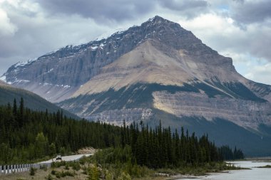 Uzun, engebeli dağlar huzurlu bir göl ve sık bir orman üzerinde yükselir. Dolambaçlı bir yol kıyı şeridini takip eder, gezginleri bulutlu bir öğleden sonra doğanın güzelliğini keşfetmeye davet eder..