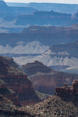Kanyon parlak öğle vakti gökyüzü altında nefes kesici jeolojik oluşumlarını gözler önüne seriyor, yüksek bir bakış açısıyla çeşitli kaya katmanlarını ve derin vadileri vurguluyor..