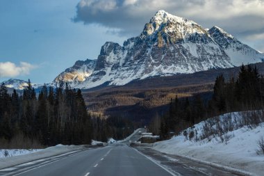Rocky dağları kışın sakin bir yol üzerinde kuleye çıkar, karlar manzarayı kaplar ve gökyüzünde dağınık bulutlar oluşturur, sakin, resim gibi bir ortam yaratır..