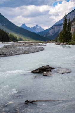 Huzurlu bir nehir, dramatik bir gökyüzünün altında yükselen dağlarla çevrili yemyeşil bir vadiden geçiyor. Temiz su, canlı bir atmosferi yansıtıyor ve sakin bir atmosfer yaratıyor..