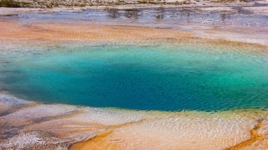 Çarpıcı bir jeotermal kaplıca, temiz bir su havuzunu çevreleyen çarpıcı mavi ve turuncu tonlarını ortaya çıkarıyor. Bu canlı doğa olayı ulusal bir parkta, ziyaretçilerin ilgisini çekiyor..