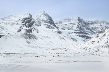 Karla kaplı engebeli dağ manzarası, keskin tepeler ve berrak gökyüzünün altında geniş bir vadi sergileniyor. Saf ayar, kış dinginliğinin özünü yakalar..