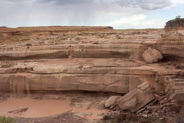 Eşsiz bir jeolojik manzara, aşağı süzülen suyla kaplı katmanlı kaya oluşumlarını içerir. Tepemizde kara bulutlar beliriyor, öğleden sonra gökyüzünde muhtemel yağmuru işaret ediyor..