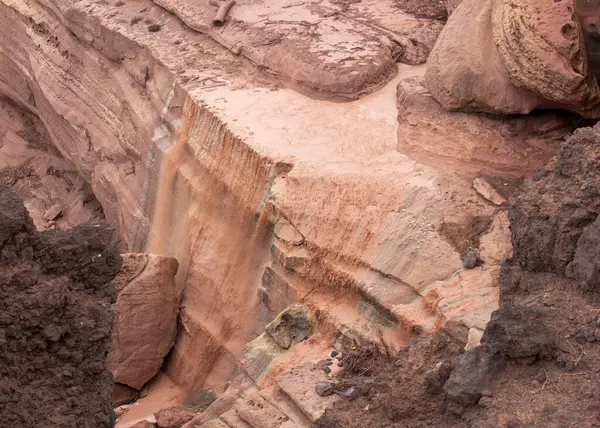 Çarpıcı bir şelale, sarp ve aşınmış kaya oluşumlarıyla çevrili engebeli bir uçurumdan zarifçe akar. Sıcak renkler bu ıssız çölün huzurlu güzelliğini vurgular..