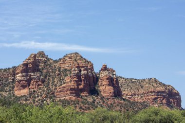 Sedona, Arizona 'da açık mavi gökyüzüne karşı eşsiz kırmızı kaya oluşumları kulesi. Manzara, yemyeşil ve güneş ışığıyla çevrili manzaranın güzelliğini yakalar..