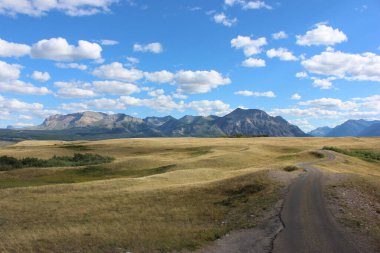 Dolambaçlı toprak bir yol altın çayırlar boyunca uzanır. Gün boyunca bulutlarla dolu berrak bir gökyüzünün altındaki uzak dağlara hakim olur..