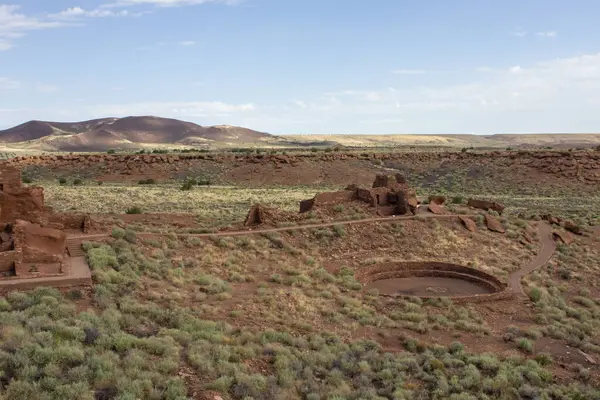 Eski bir medeniyetin kalıntıları kuru bir çöl arazisine saçılmış, taş yapılar açık bir gökyüzünün altında çalıların ve uzak dağların arasında görülebiliyor..