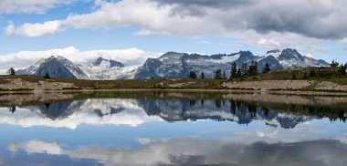 Göz kamaştırıcı bir dağ silsilesi karla çevrili zirvelerle görülebilir. Sakin bir göl, parlak bir gökyüzünün altındaki dağları ve bulutları mükemmel bir şekilde yansıtır ve sakin bir atmosfer yaratır..