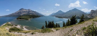 Nefes kesici bir manzara, yemyeşil yemyeşil ve parlak mavi gökyüzünün altında yükselen dağlarla çevrili sakin bir göle sahiptir. Sakin sular, etrafındaki güzelliği yansıtır ve güzel bir manzara yaratır..