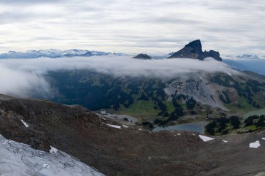 Dramatik manzara, sabahın erken saatlerinde yemyeşil vadileri ve dingin gölleri olan bulutlardan oluşan bir battaniyenin üzerinde yükselen engebeli bir dağ siluetini yansıtıyor..