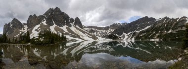 Sakin bir gölün üzerindeki görkemli dağ tepeleri yansımaları çarpıcı bir ayna etkisi yaratıyor. Yeşillik suları sarar ve doğal güzellikleri artırır..