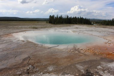 Sıcak kaynak, Yellowstone Ulusal Parkı 'ndaki turuncu ve sarı mineral yataklarıyla çevrili canlı mavi suyu gösteriyor..
