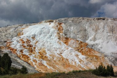 Ziyaretçiler Yellowstone Ulusal Parkı 'ndaki Mammoth Kaplıcaları' ndaki mineral yataklarının oluşturduğu büyüleyici teraslara hayret ediyorlar. Eşsiz renkler dramatik bulutlu gökyüzüne karşı kontrasttır.