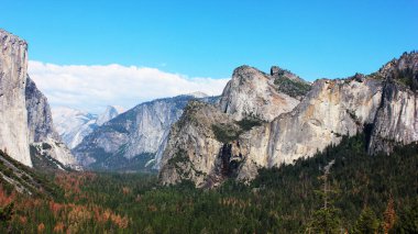 Sık yeşil bir ormanı çevreleyen granit kayalıklar nefes kesen manzara gösterileri. Yosemite Ulusal Parkı. Manzaralı vadi, doğayı ve huzuru harmanlayan mesafeye kadar uzanıyor..