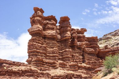 Alışılmadık kırmızı kaya oluşumları parlak mavi gökyüzüne karşı haşmetli bir şekilde yükseliyor. Gün boyunca bu çarpıcı açık havada kumtaşı katmanları sergiliyorlar..