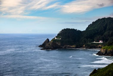 Dalgalar Oregon kıyısı boyunca kayalık kayalıklara çarpar. Huzurlu suların üzerinde duran ve yemyeşil sularla çevrili tarihi bir deniz feneri vardır..