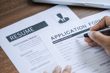Closeup hand holding pen for completing the application form with resume on the table 