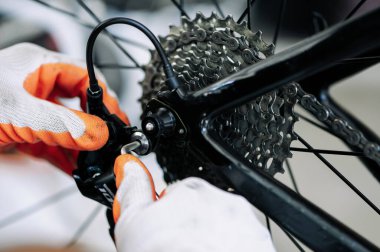 close - up of the male mechanic working in the bicycle repair shop, mechanic repairing bike using a special tool, wearing protective gloves. Bike Maintenance Concept.