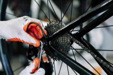 close - up of the male mechanic working in the bicycle repair shop, mechanic repairing bike using a special tool, wearing protective gloves. Bike Maintenance Concept.