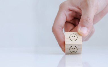 Close up of hand customer hand choose a smiley face and blurred sad face icon on the wood cube, Service rating, satisfaction concept.