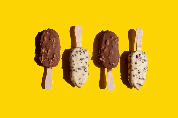 ice cream on a stick in white chocolate with cookies and in milk chocolate with nuts on a yellow background