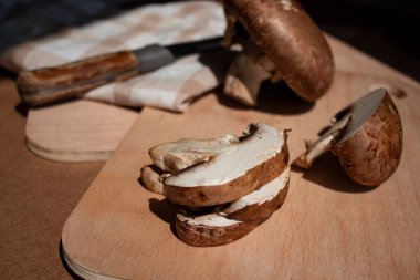 Mantarlar (kahverengi şapkalı büyük şampiyonlar) tahtanın üzerinde yatar, bir mantar kesilir ve diğeri bir bütün, yanında bir bıçak ve bir mutfak havlusu bulunur.