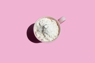 Pembe arka planda pembe bardaktaki kuru protein.