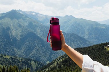 Adam elinde bir şişe tutuyor doğanın, gökyüzünün, dağların arka planına karşı.