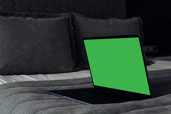 a laptop with a green screen is lying on a bed with a gray blanket