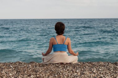 Genç bir kız, sırtını nilüfer pozisyonunda sahilde tek başına oturur.