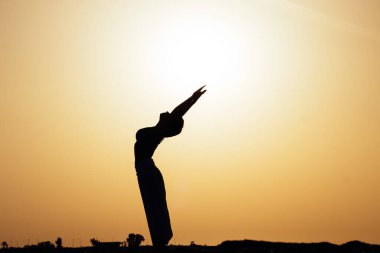 Pozitifliğe konsantre olmaya çalışan genç kadın silueti gün batımında yoga, pilates ya da güzel bir dağ yerinde gün doğumu pratiği yapıyor. Beden ve zihin rahatlığı için fiziksel aktivite, sağlıklı yaşam tarzı alışkanlıkları kavramı 