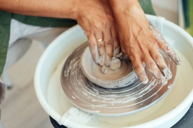 Seramik dersi, çömlekçinin tekerinde kil tabak yapan bir adam.