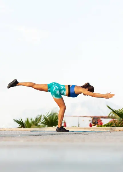 stock image sporty woman performs balance exercises against the background of the sea and mountains. doing yoga in warrior asana in the beach