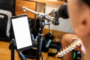 Şarkıcı akıllı telefon ekranında şarkı sözleri okuyor. Mikrofon için telefon tutacağı var. Kayıt stüdyosundaki prova sırasında müzik sanatçısı mikrofon aygıtı.
