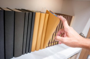 Halk kütüphanesindeki ahşap kitaplıktan kahverengi kitap seçen ve seçen bir erkek. Üniversite hayatı kavramlarında eğitim araştırmaları ve kendi kendine öğrenme