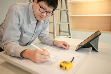 Ev tadilatı ya da tadilat. Yeni mutfak tezgahında mimari çizim ve inşaat aletleriyle çalışan Asyalı erkek iç işçisi veya mobilya toplayıcısı dijital tablet kullanıyor.