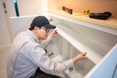 Ev tadilatı ya da ev dekorasyonu konsepti. Asyalı erkek mobilya derleyicisi ya da iç inşaat işçisi dolapta beyaz raf paneli kuruyor. Yeni ev için mobilya kurulumu.