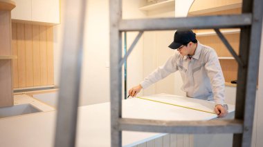 Ev tadilatı ya da ev dekorasyonu konsepti. Asyalı erkek mobilya derleyicisi ya da inşaat işçisi yeni mutfağın tezgahında mezura kullanıyor..