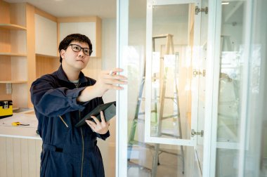 Ev tadilatı ya da ev dekorasyonu konsepti. Asyalı erkek inşaat işçisi veya mobilya toplayıcısı dijital tablet kontrol paneli kullanarak kabine kurulumunu kontrol ediyor.