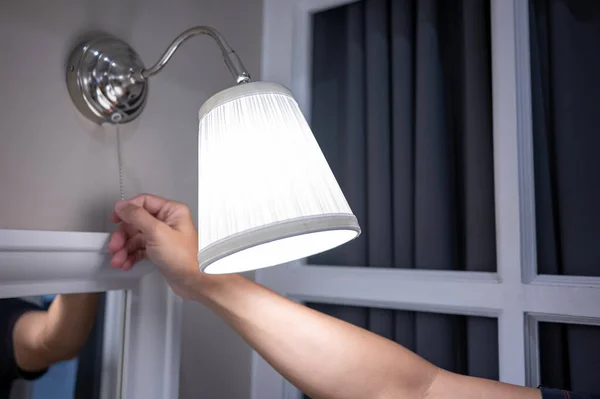 stock image Male hand turn off the light on wall lamp in bedroom. Saving electricity energy at night. Switch off lighting equipment for bedtime.