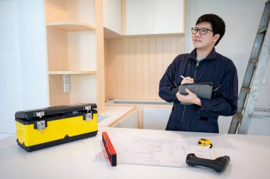 Ev tadilatı ya da tadilat. Asyalı erkek içişleri çalışanı dijital tablet kullanıyor ve mutfak tezgahında inşaat aletleriyle çalışıyor. Mobilya montajcısı yeni ev için dolap kuruyor.