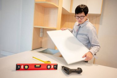 Ev tadilatı ya da ev dekorasyonu konsepti. Asyalı erkek mobilya derleyicisi ya da inşaat işçisi mutfak tezgahına dolap paneli yerleştiriyor. Yeni ev için mobilya kurulumu.