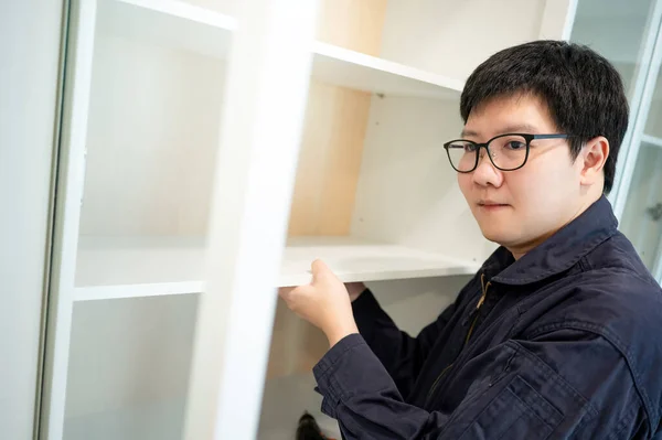 Home renovation or House remodeling concept. Asian male furniture assembler or Interior construction worker man installing white shelf panel in the cabinet. Furniture installation for the new house.