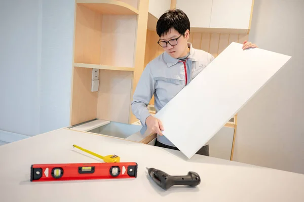 Home renovation or House remodeling concept. Asian male furniture assembler or Interior construction worker man installing cabinet panel on kitchen counter. Furniture installation for the new house.