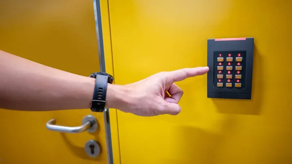 Male finger entering password code number on numeric keypad of smart electronic digital door lock on yellow wall. Security and privacy concept