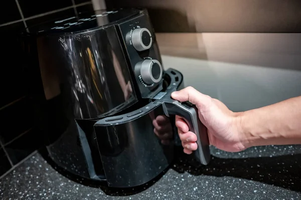 Stock image Male hand holding an electric air fryer handle in the kitchen. Home appliance for healthy cooking lifestyle.