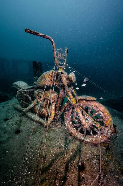 Underwater scene of submerged rusty motorcycle used as artificial coral reef at Tor 13 dive site or the underwater museum in Andaman sea, Thailand.