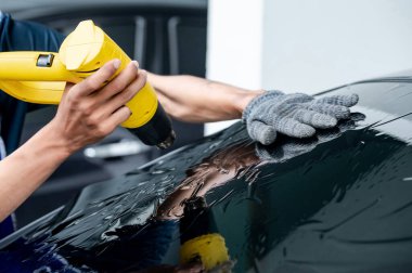 Otomobil uzmanı el fön makinesi ya da saç kurutma makinesi eski arabanın cam boyasını çıkarıp yenisini takıyor. Araba ön cam film kaldırma ve boyama kurulumu