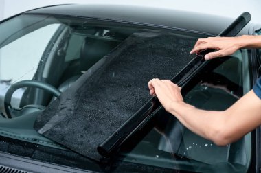 Erkek otomobil uzmanı el kamerasıyla ön cam yüzeyinde film çekiyor. Araba kenarı film kaldırma ve boyama kurulumu. 